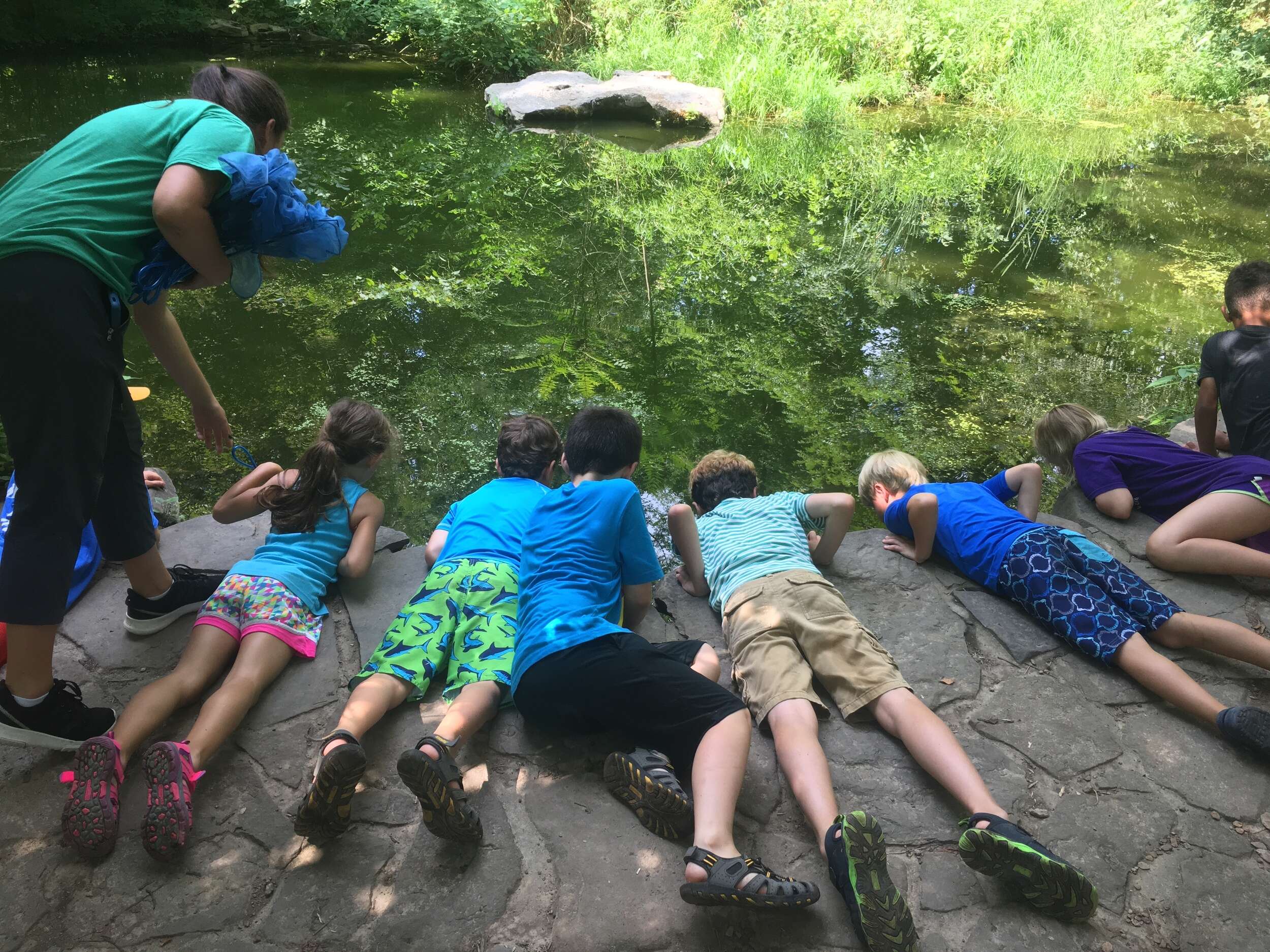 Group of children laying on rock looking into water - Leadership Academy